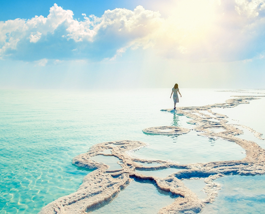 Eine Frau im weißen Kleid spaziert über einen Strand